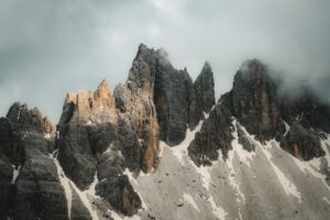 Rugged alpine peaks with patches of snow under a gray cloudy sky, creating a dramatic mountain landscape.